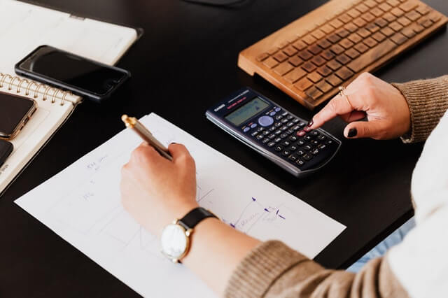 Person doing bookkeeping duties wearing a watch and typing in calculator.