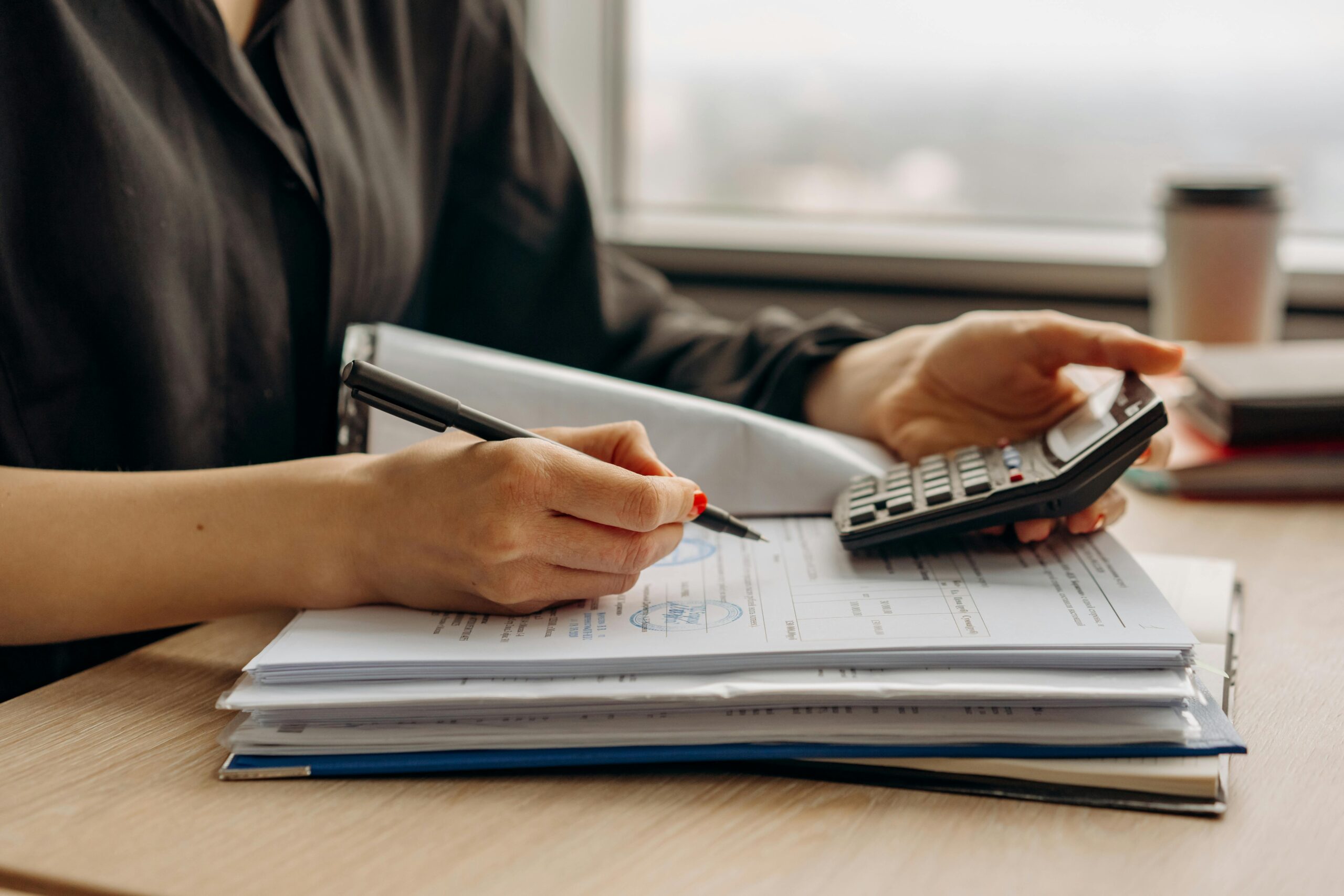 Woman writing and looking at calculator with long sleeves